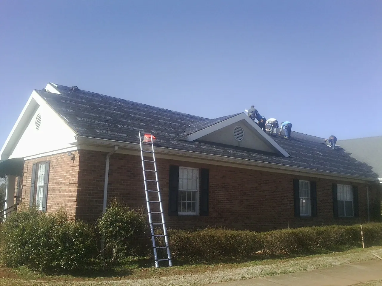 Crew tearing shingles off a brick ranch roof with a ladder set — Emergency Roof Repair work by our crew in Saint Paul