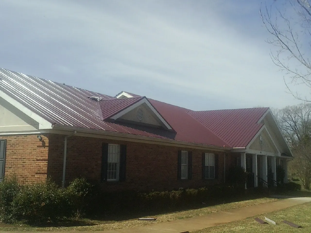 Red metal roof with gabled entries on a long brick building, from a Hail Damage Roof Repair job in Saint Paul
