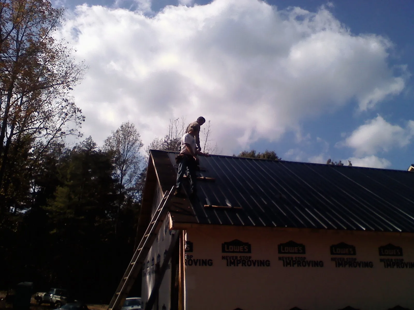 Roofer fastening dark metal panels high against a cloudy sky, from a Roof Inspection job in Saint Paul