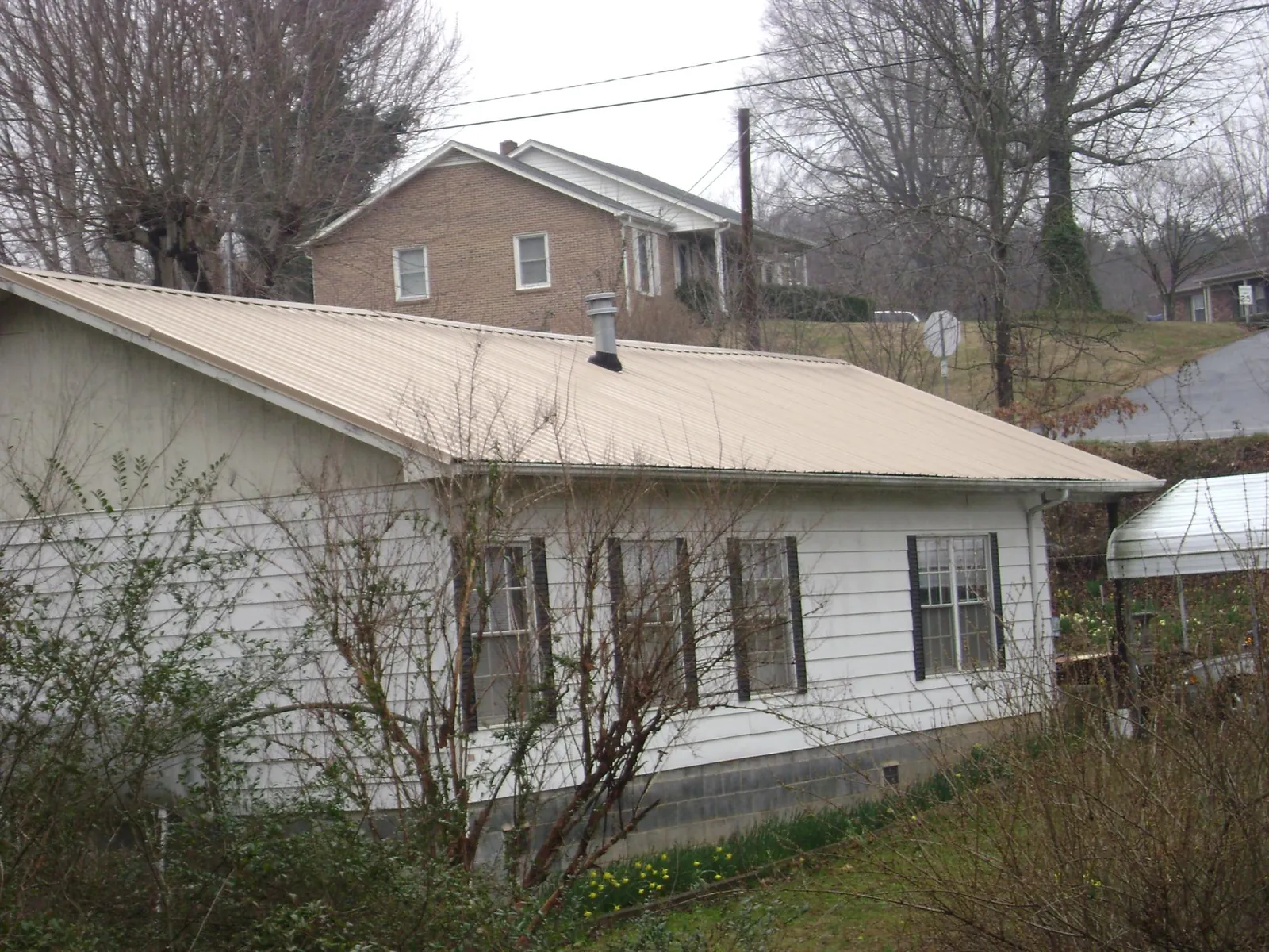 Tan metal roof on a white sided house set into a hillside — Commercial Roofing by Roofing Brothers in Saint Paul