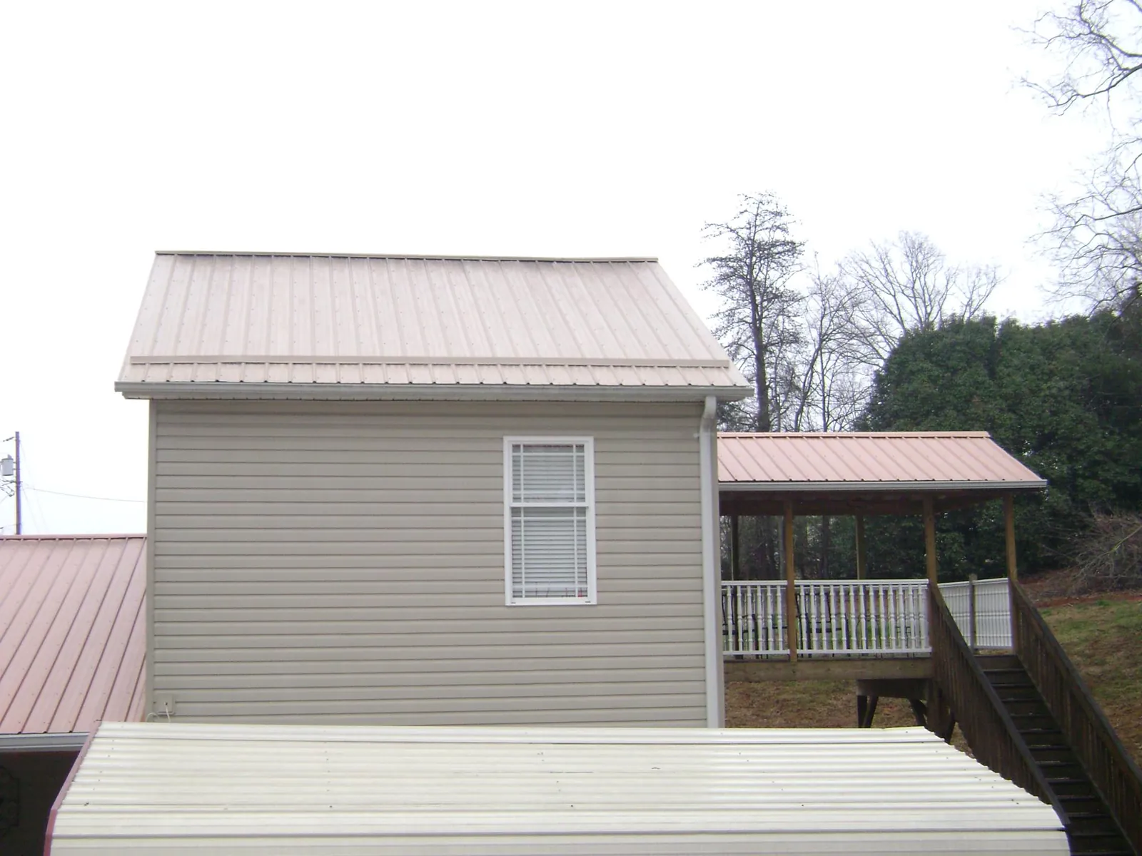 Tan metal roofs on a two story addition and attached porch, from a Roof Replacement job in Saint Paul